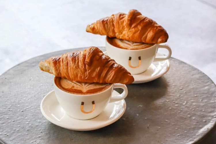 Two cups of coffee with croissants on top of them