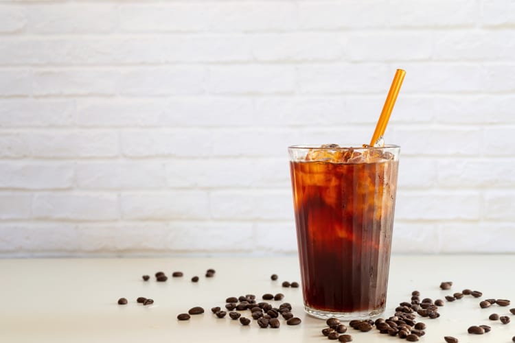 Eye-level view of a cold brew iced coffee surrounded by coffee beans