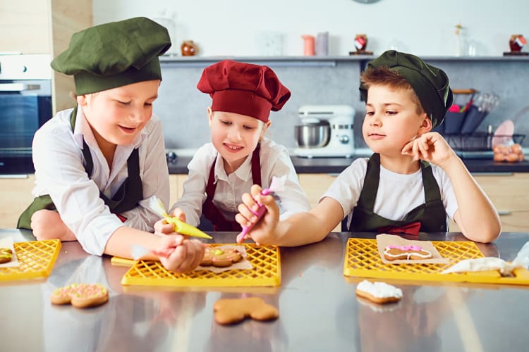 Three young boys wearing chefs hats decorating cookies