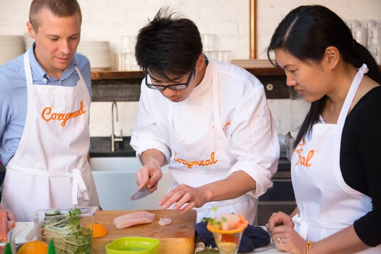 Two people taking a cooking class with an expert chef, booked through Cozymeal