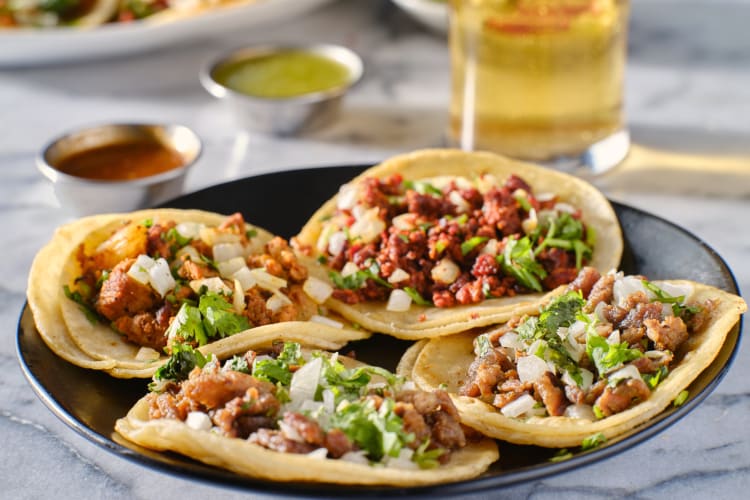 Four corn tortillas in a bowl with mince and other fillings in them