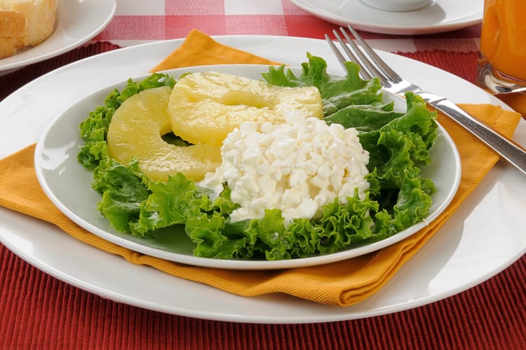 Cottage cheese on a bed of greens next to two pineapple rings