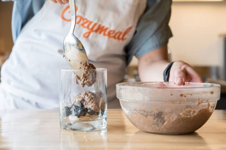 A chef in a Cozymeal apron putting chocolate mousse in a glass