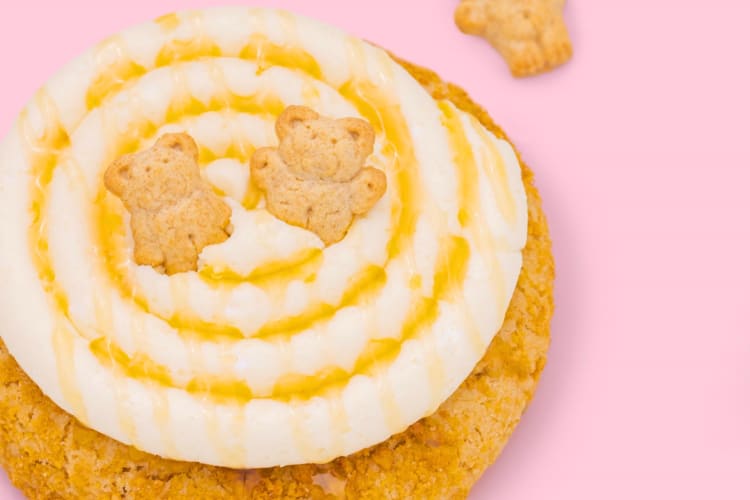 A cookie with frosting and two Teddy Grahams on a pink background