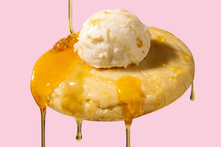A cornbread cookie with butter frosting and honey on a pink background