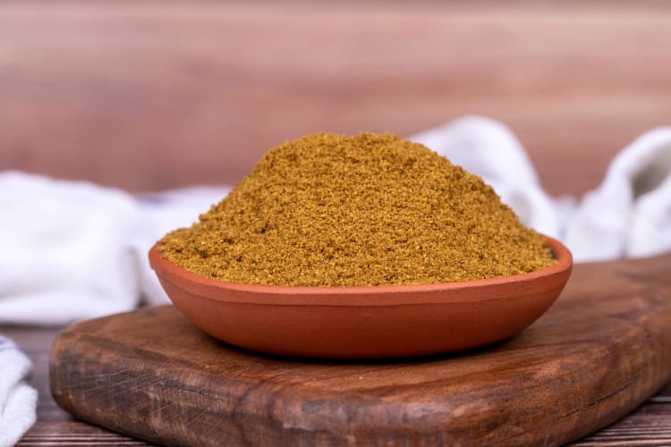 A bowl of ground cumin on a wooden board