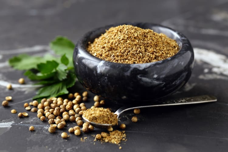 A black bowl with ground coriander next to fresh coriander