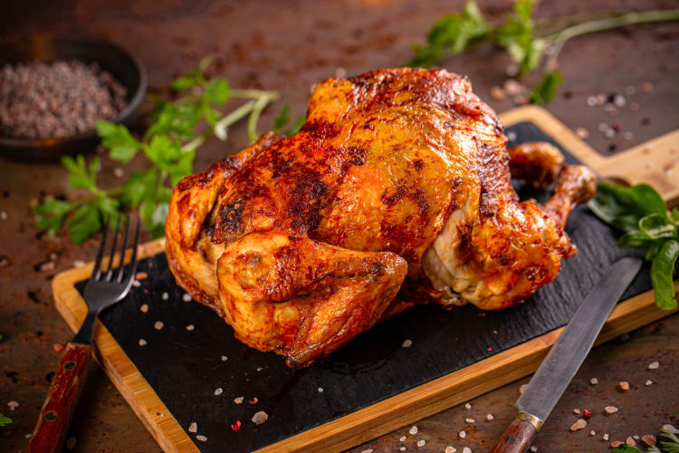 Whole chicken on a cutting board in between a knife and fork