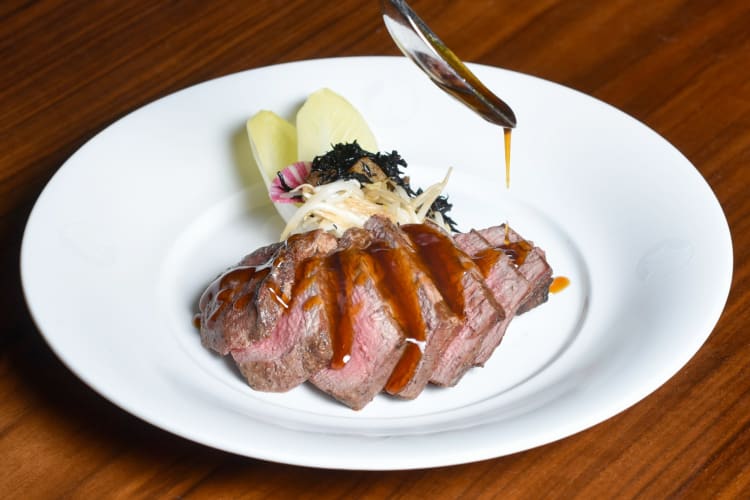 A person pouring sauce onto a meat and endive dish