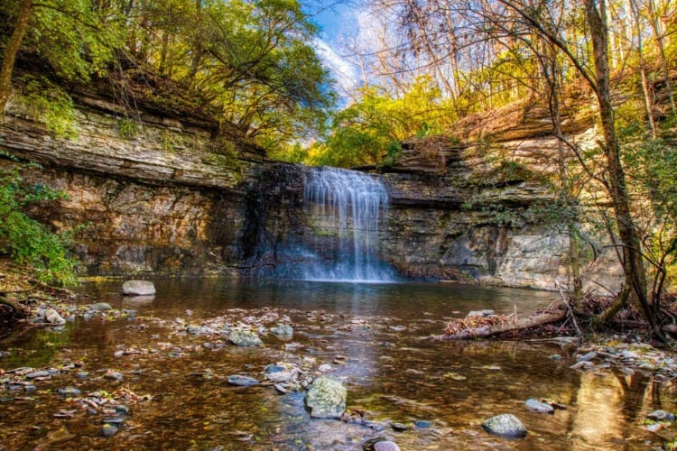 A waterfall flowing into a river surrrounded by rocks and trees