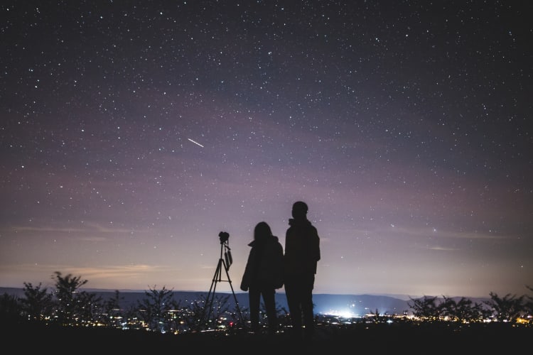 The shadows of two people next to a purple starry night sky