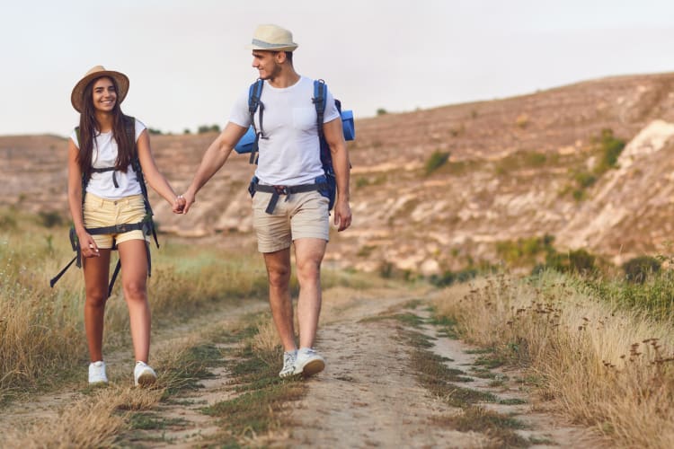 A couple walking on a sandy path near hills