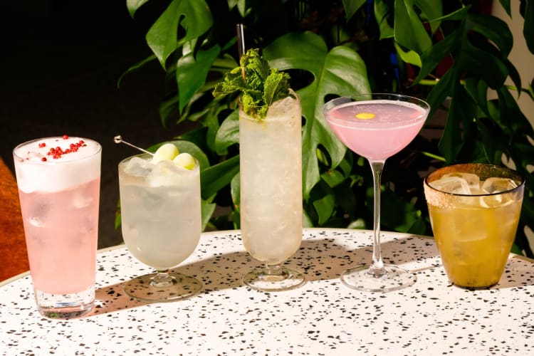 Five cocktails on a terrazzo table next to greenery