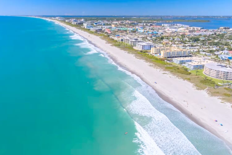 An aerial view of a beach with blue ocean, white sand and buildings