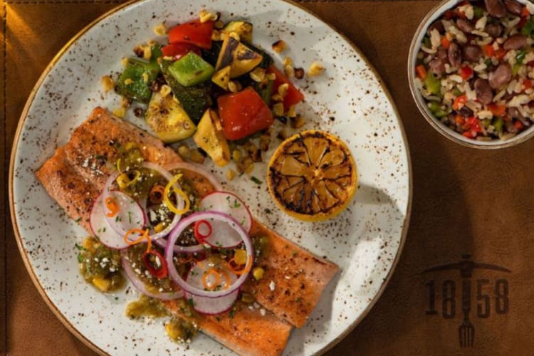 A salmon dish on a leather mat next to a bowl with rice and beans