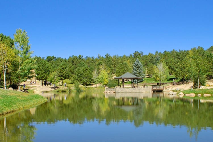 A small bandstand in a green park next to a lake