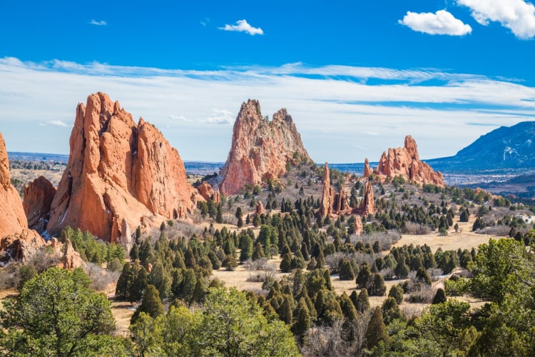 Red rock mountains and green trees under a blue sky with clouds