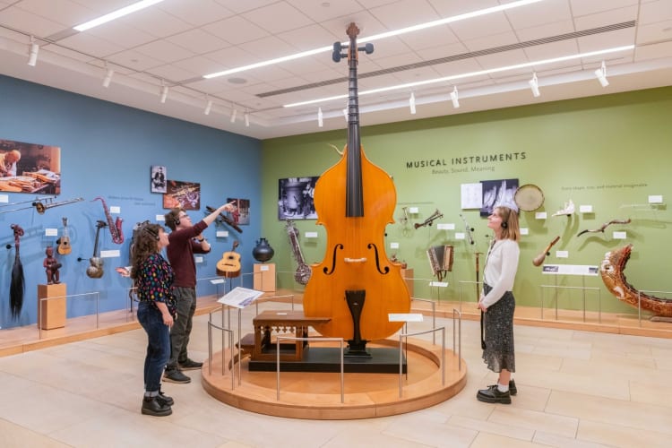 A museum exhibit with many musical instruments and three people looking at them