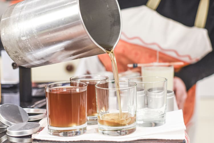 A person pouring melted wax into candle jars