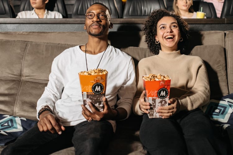 A couple on a couch in a movie theater with popcorn