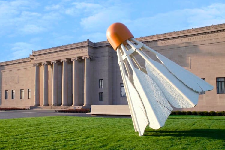 A shuttlecock statue next to a large stone museum