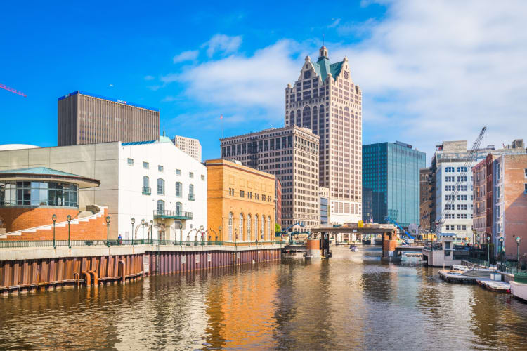 A river next to city buildings and a bright blue sky with clouds