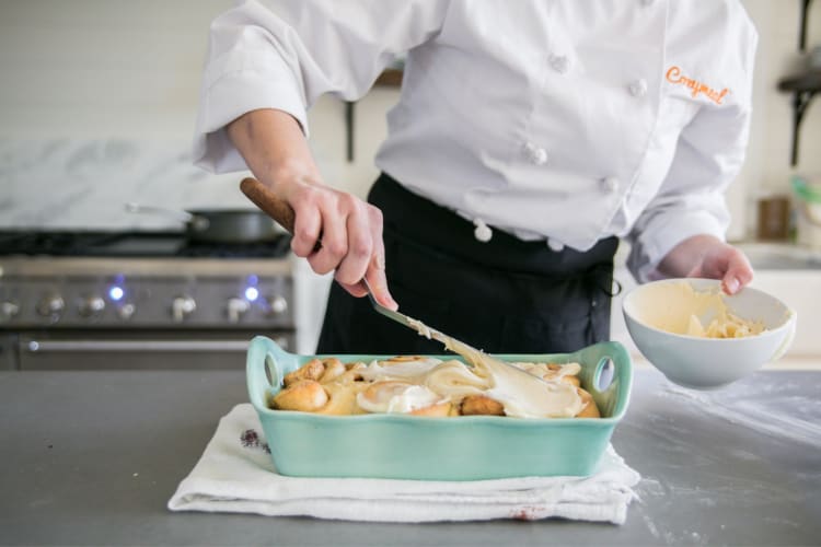 A chef in a Cozymeal apron putting frosting on cinnamon buns