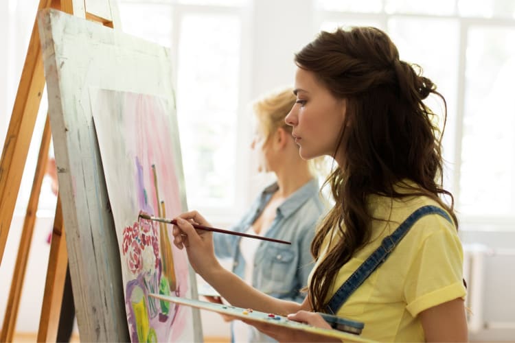 A woman painting on a canvas on an easel 