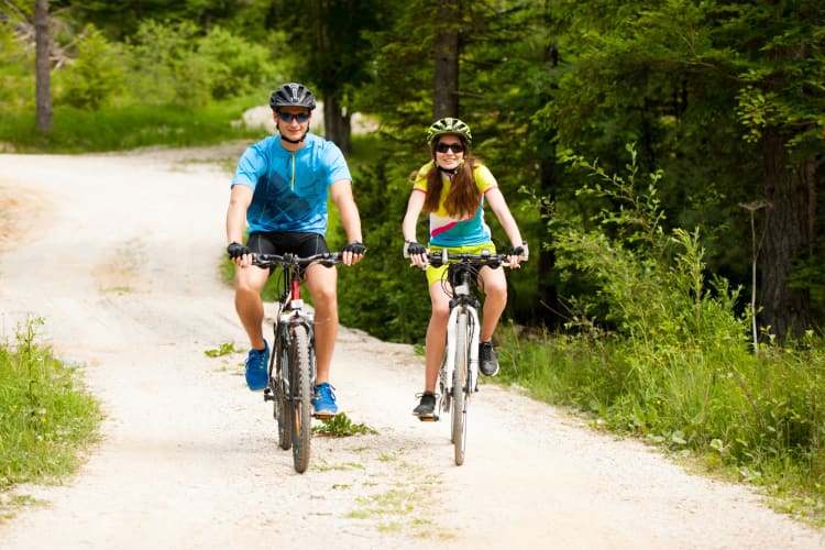 A couple riding bikes on a bike trail surrounded by trees