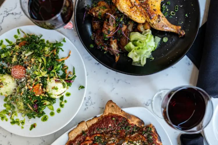 A chicken dish, salad, pizza and glasses of red wine on a table