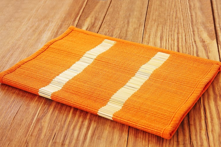 Bright orange placemat with two white stripes, on a wooden surface