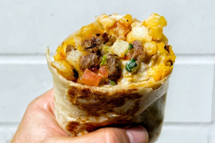 A person holidng a burrito with fries, meat and vegetables