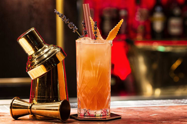A cocktail on a bar next to a gold cocktail shaker