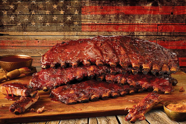 Side-view of racks of ribs in front of an American flag painted on wooden panels