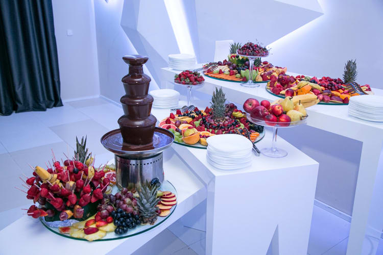 Chocolate fountain surrounded by platters of fruit and plates
