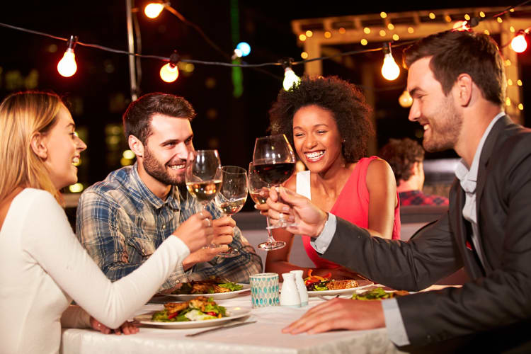 Four friends clinking wine glasses together while at a restaurant