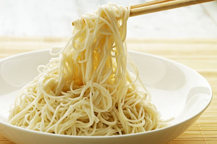 A person picking up plain noodles from a bowl with chopsticks