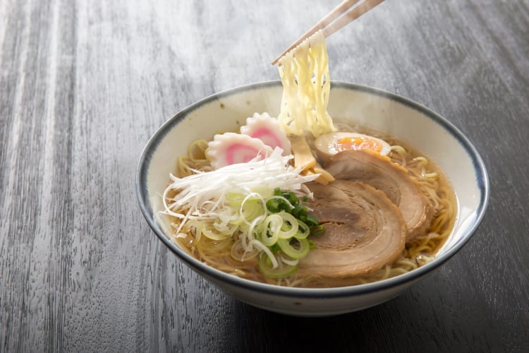 A person picking up noodles with chopsticks from a bowl of ramen