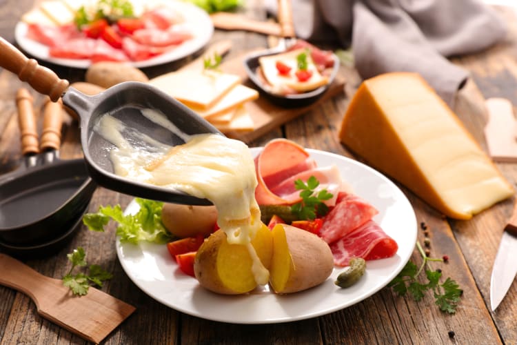 Melted cheese from a pan being poured over potatoes on a plate with meats and vegetables