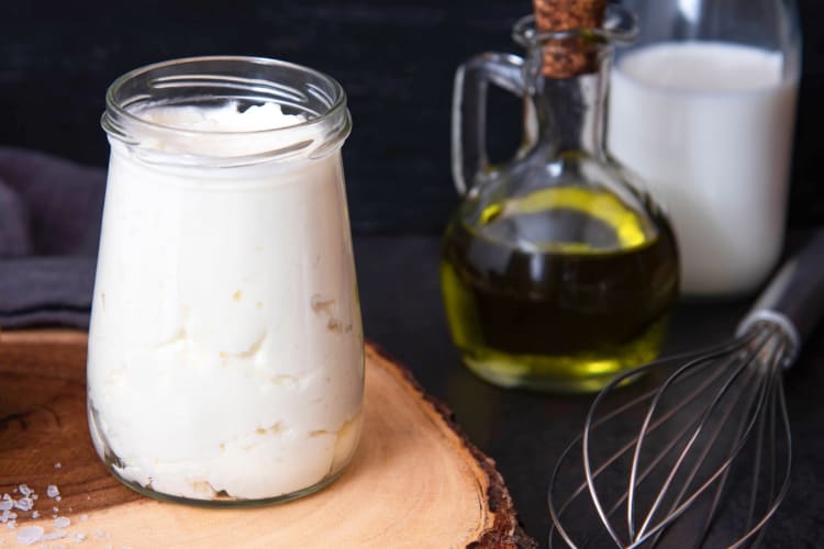 A glass jar with mayonnaise next to a whisk and olive oil