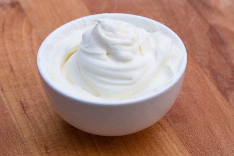 Sour cream in a white bowl on a wooden surface