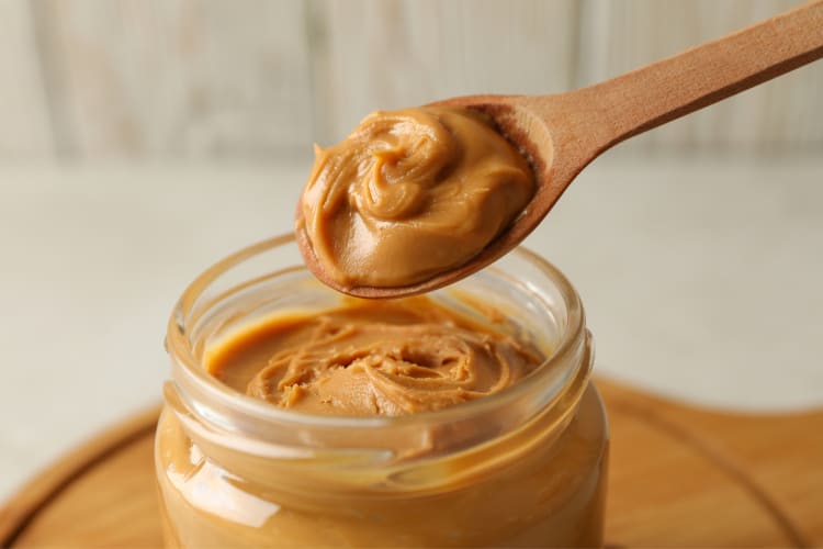 A spoon with peanut butter above a jar of peanut butter