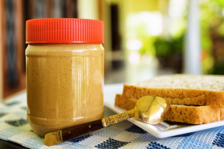 A jar of peanut butter with a red lid next to bread 