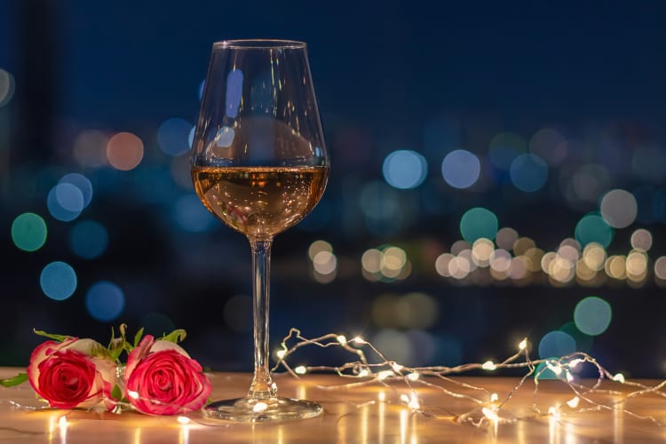 A glass of wine in between string lights and two roses