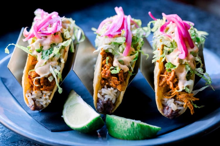 Three tacos with lime on a blue plate