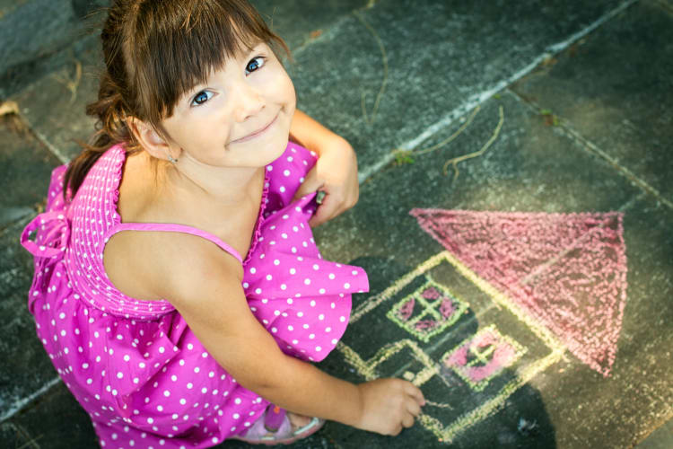 Little girl using chalk to draw a house on the sidewalk