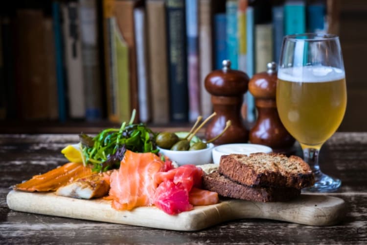 Fish on a wooden board next to a pint of beer