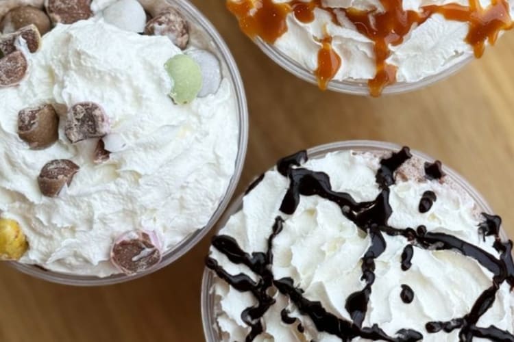 Three Dunkin' Donuts drinks topped with whipped cream, syrup and chocolate pieces.