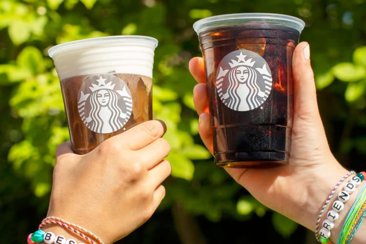 Two people holding Starbucks coffee drinks