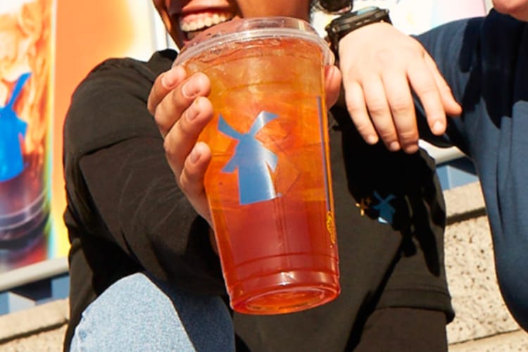 A person holding an orange drink in a clear takeout cup